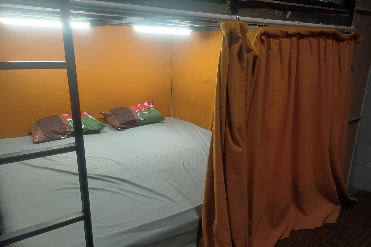 Un lit superposé avec un matelas blanc, des rideaux orange et des coussins décoratifs.