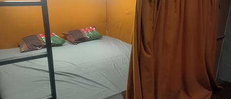 A bunk bed with a white mattress, orange curtains, and decorative pillows.