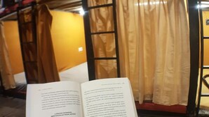Una persona leyendo un libro en una habitación con piso de madera y cortinas color beige.
