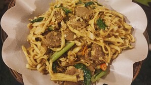 Un tazón de fideos con carne y verduras, servido en un plato de papel.