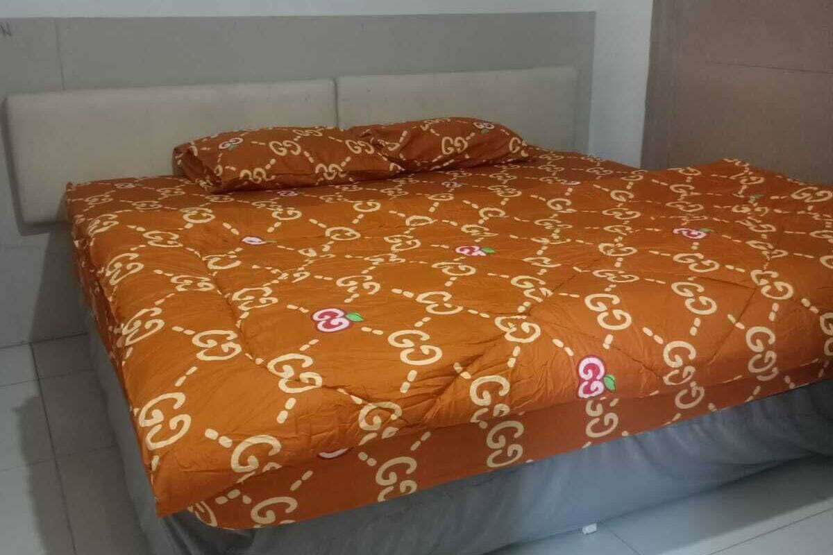 Un lit avec une couvre-lit à motifs et des oreillers, une tête de lit et un sol carrelé.