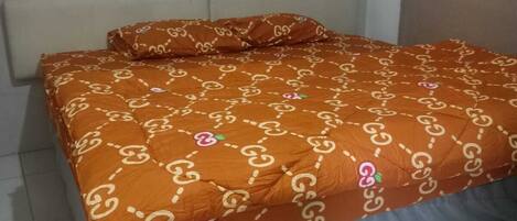 Una cama con una colcha estampada y almohadas, un cabecero y un suelo de baldosas.