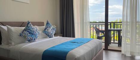 A hotel room with a large bed, a view of the outdoors, and a balcony with a table and chairs.