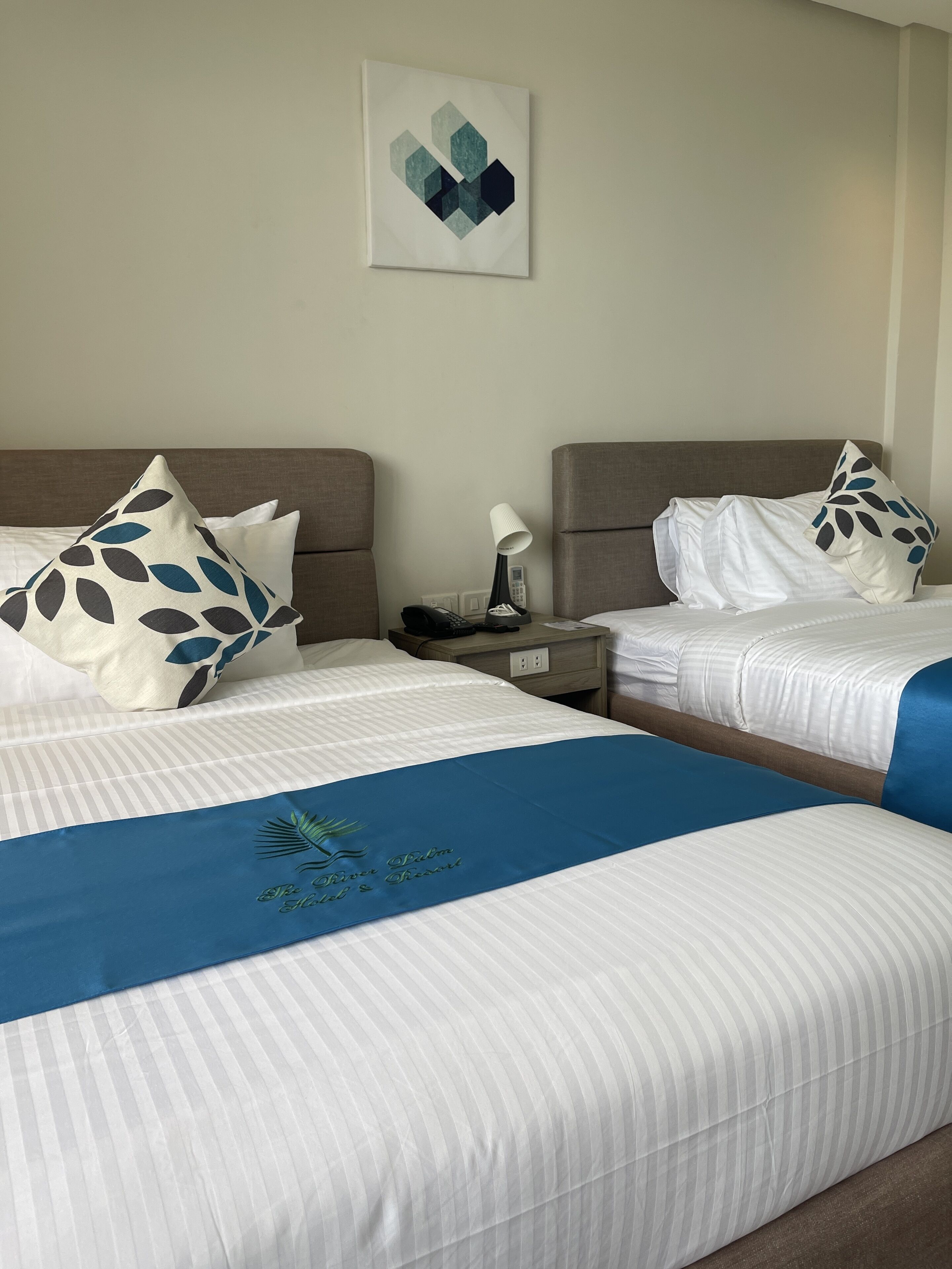 A hotel room with two beds, each with a pillow and a bedside table with a lamp and phone.