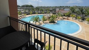 Un balcón con vista a una piscina, palmeras y un cielo despejado.