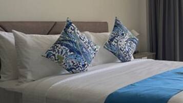 A hotel room with a bed, pillows, a blue blanket, and a painting on the wall.