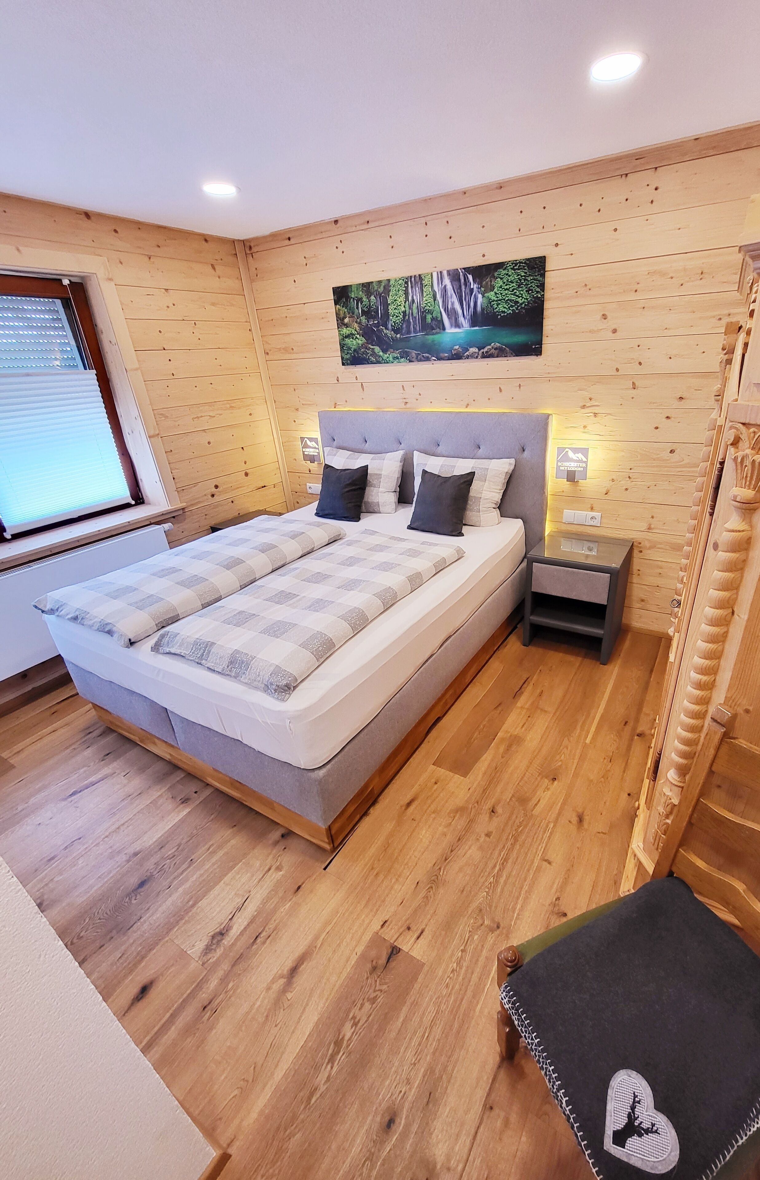 Una camera da letto moderna con un letto grande, pareti in legno, un quadro raffigurante una cascata e un comodino.