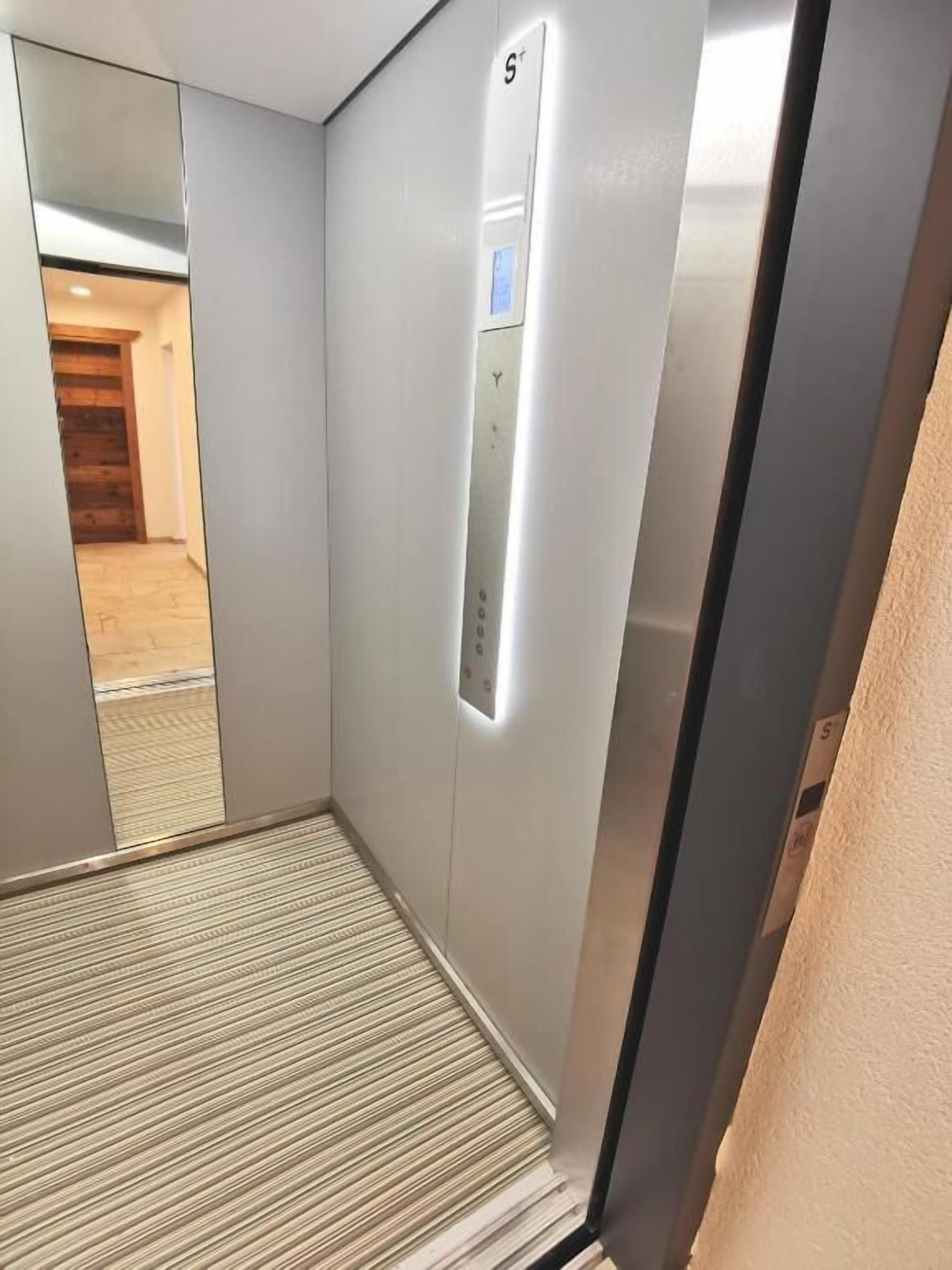 An elevator interior with a control panel, a striped floor, and a wooden door at the end.