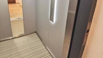 An elevator interior with a control panel, a striped floor, and a wooden door at the end.
