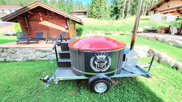 A portable VIP hot tub with a red cover, a metal frame, and a logo, set on a grassy area with a wooden deck and chairs in the background.