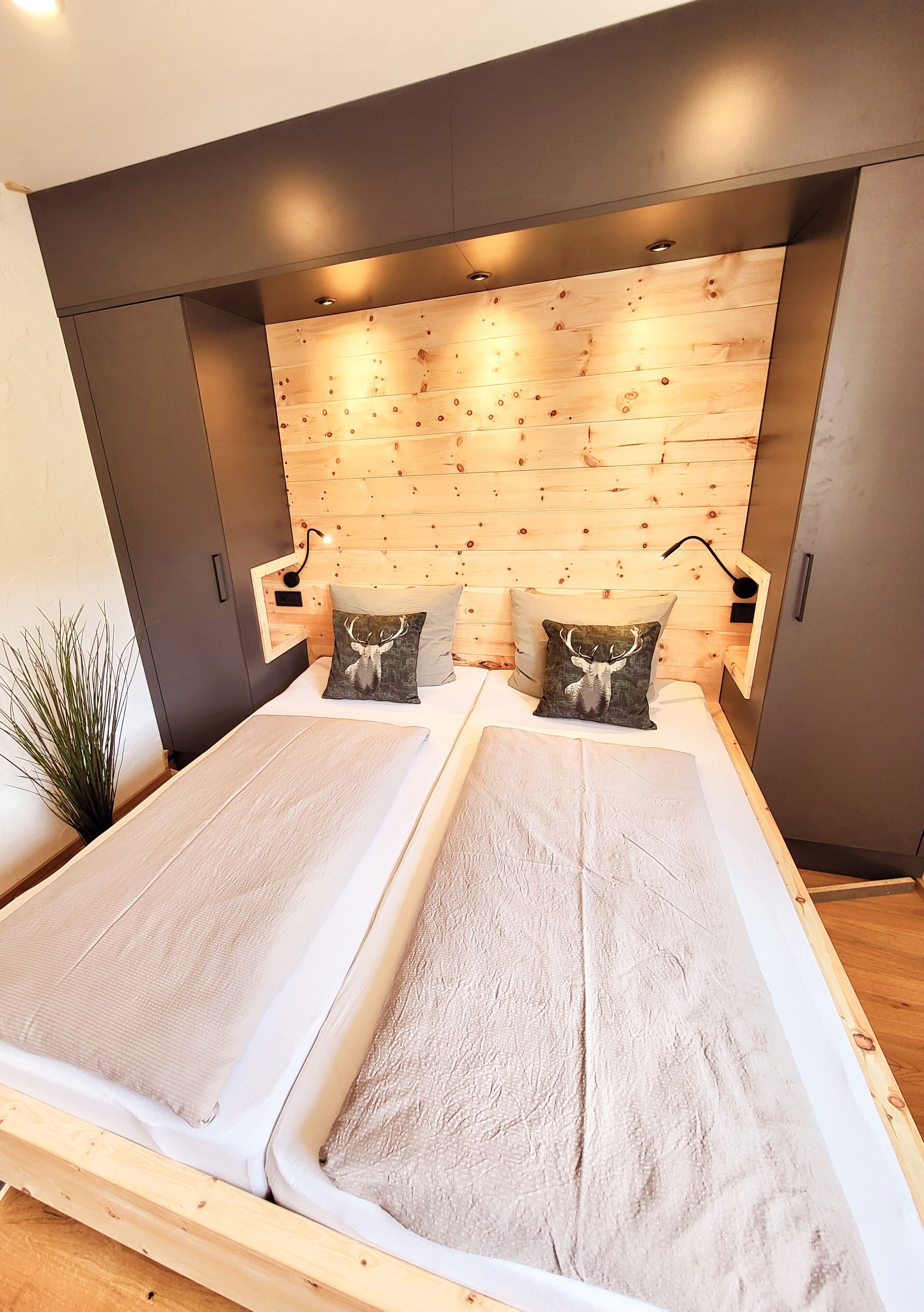 A modern bedroom with a wooden headboard, two beds, and a small plant.
