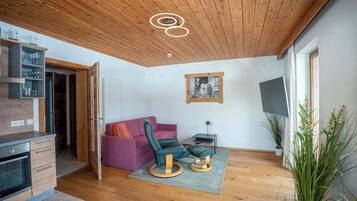 Un soggiorno moderno con soffitto in legno, un divano, una poltrona verde, una TV e un tavolino.