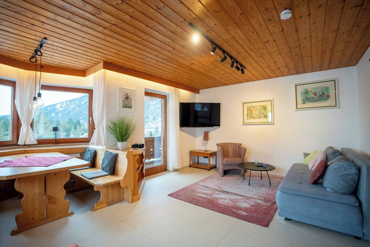 Una sala de estar acogedora con techo de madera, un sofá, un televisor y un comedor con mesa y sillas.