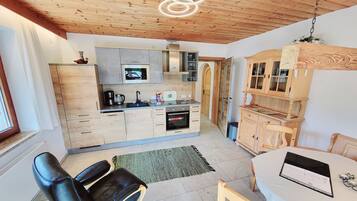A modern kitchen with wooden cabinets, a built-in microwave, and a coffee maker. There is a dining area with a table and chairs, and a laptop on the table.