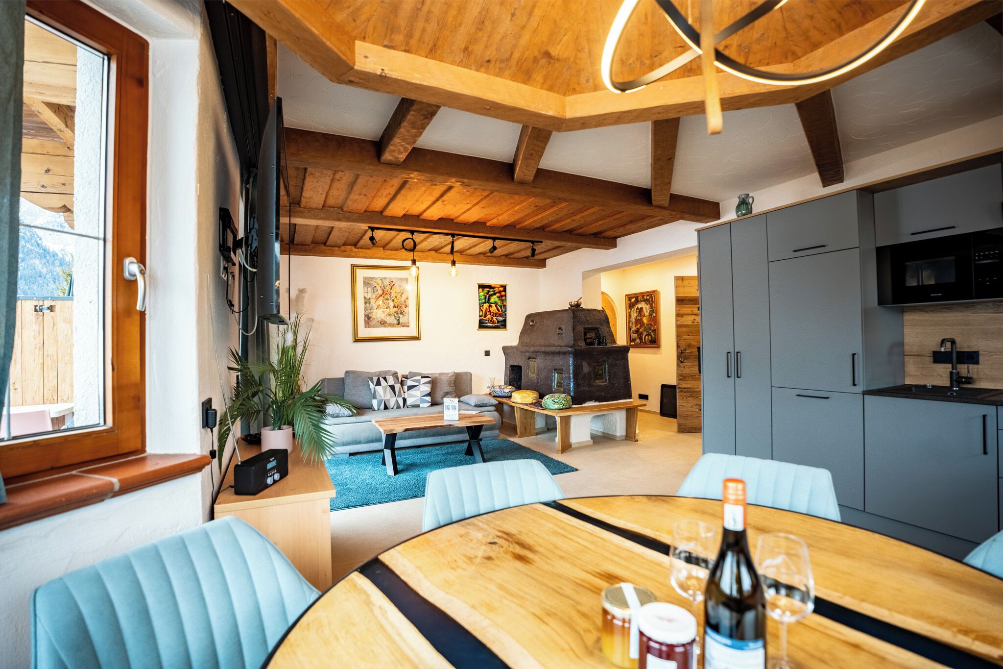 A cozy living area with a wooden ceiling, a dining table with chairs, a sofa, and a kitchen area with cabinets and appliances.
