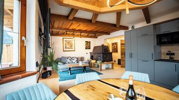 A cozy living area with a wooden ceiling, a dining table with chairs, a sofa, and a kitchen area with cabinets and appliances.