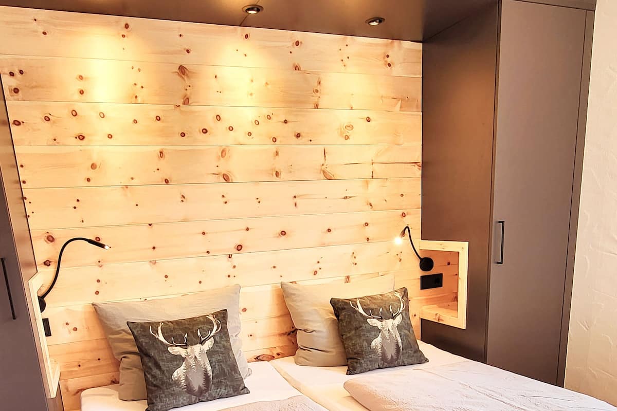 Un dormitorio moderno con cabecera de madera, dos camas con ropa de cama blanca y almohadas decorativas.