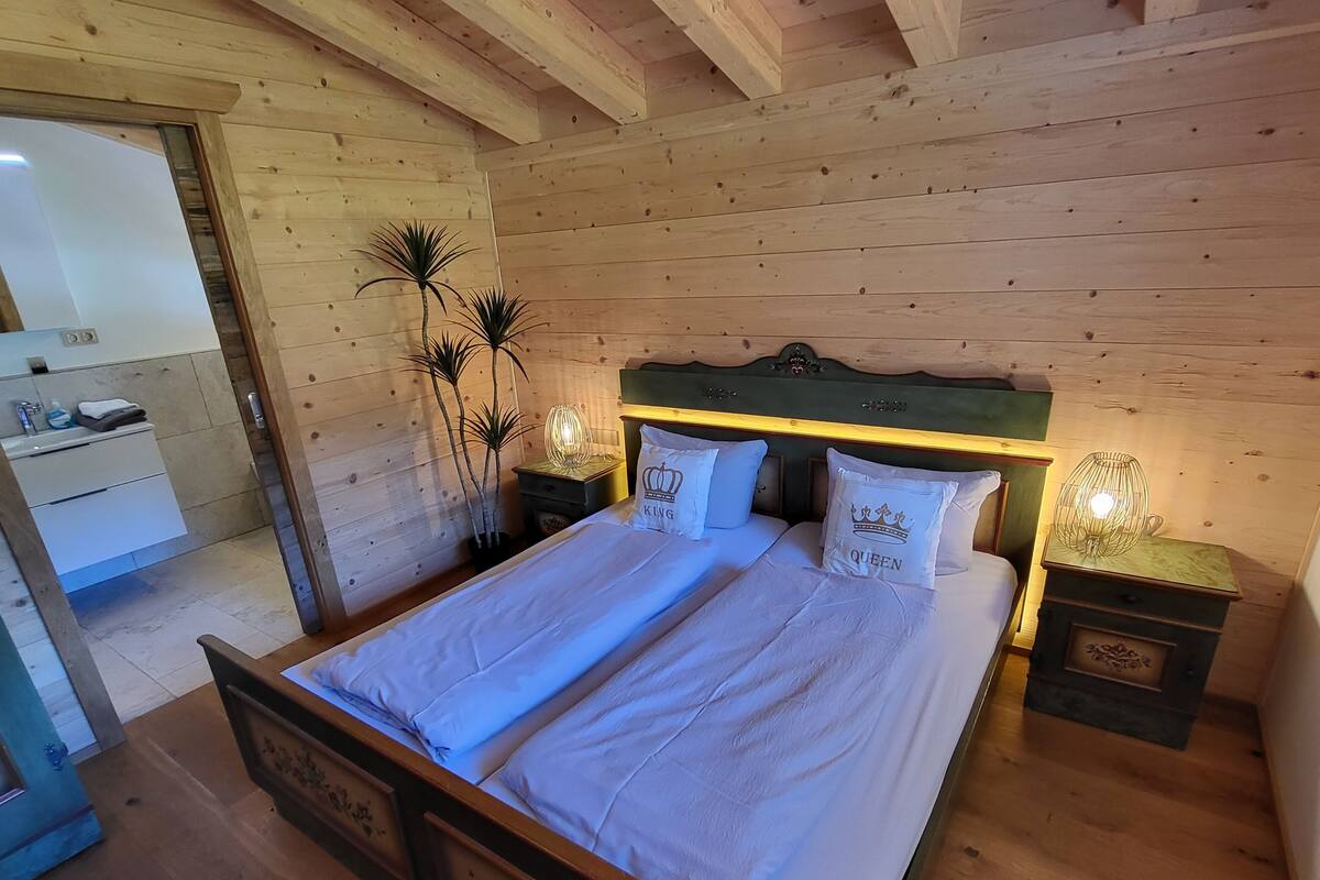Un dormitorio con paneles de madera, una cama doble, dos mesitas de noche y una mesita de noche con lámpara.