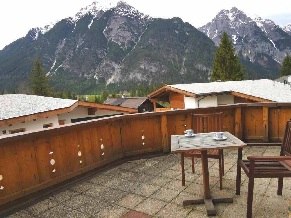 Una terrazza in legno con tavolo e sedie, affacciata su un paesaggio montano.
