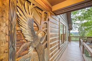 A wooden cabin with a detailed carved eagle on the exterior wall, a wooden deck, and a view of the surrounding landscape.