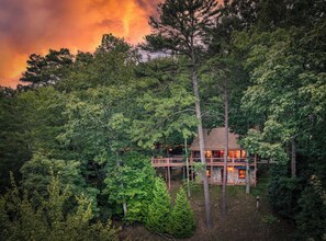 A cabin surrounded by dense forest, with a deck extending over a body of water.