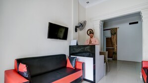 Ein modernes Wohnzimmer mit einer schwarz-roten Couch, einem Flachbildfernseher, einem an der Wand befestigten Ventilator und einer Treppe, die in einen anderen Bereich führt.