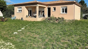 A two-story house with a tiled roof, a covered patio, and a grassy yard.