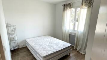Un dormitorio con una cama individual, un radiador, una ventana con cortinas y una puerta.