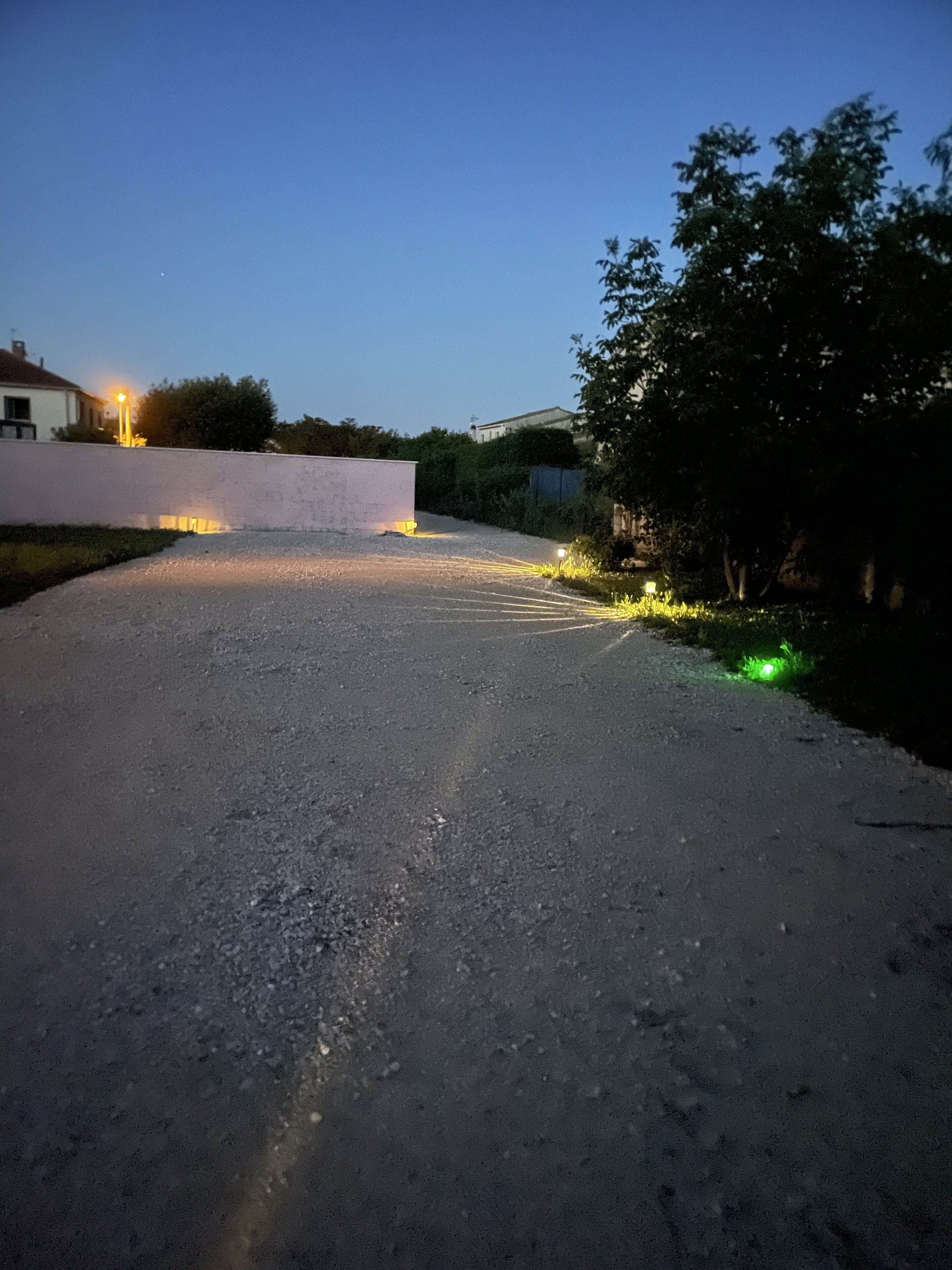 A paved driveway leading to a white building with a light source on the left.