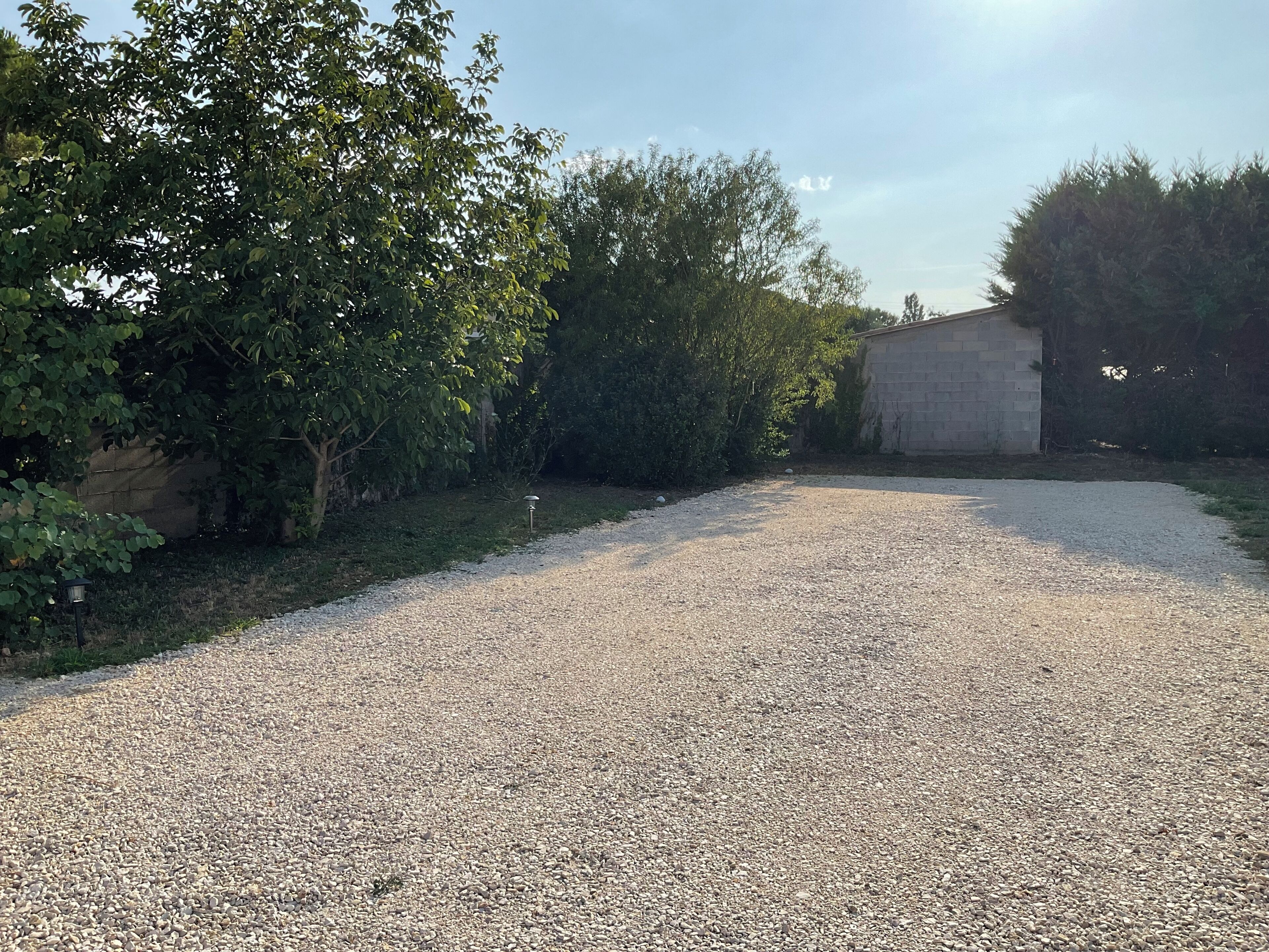 A gravel driveway leading to a building with a stone wall and dense foliage on one side.