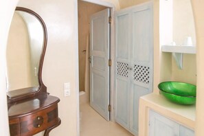 A hallway with a wooden dresser, a mirror, and a green bowl on a countertop. - Kastro Oia Houses  (Santorini)