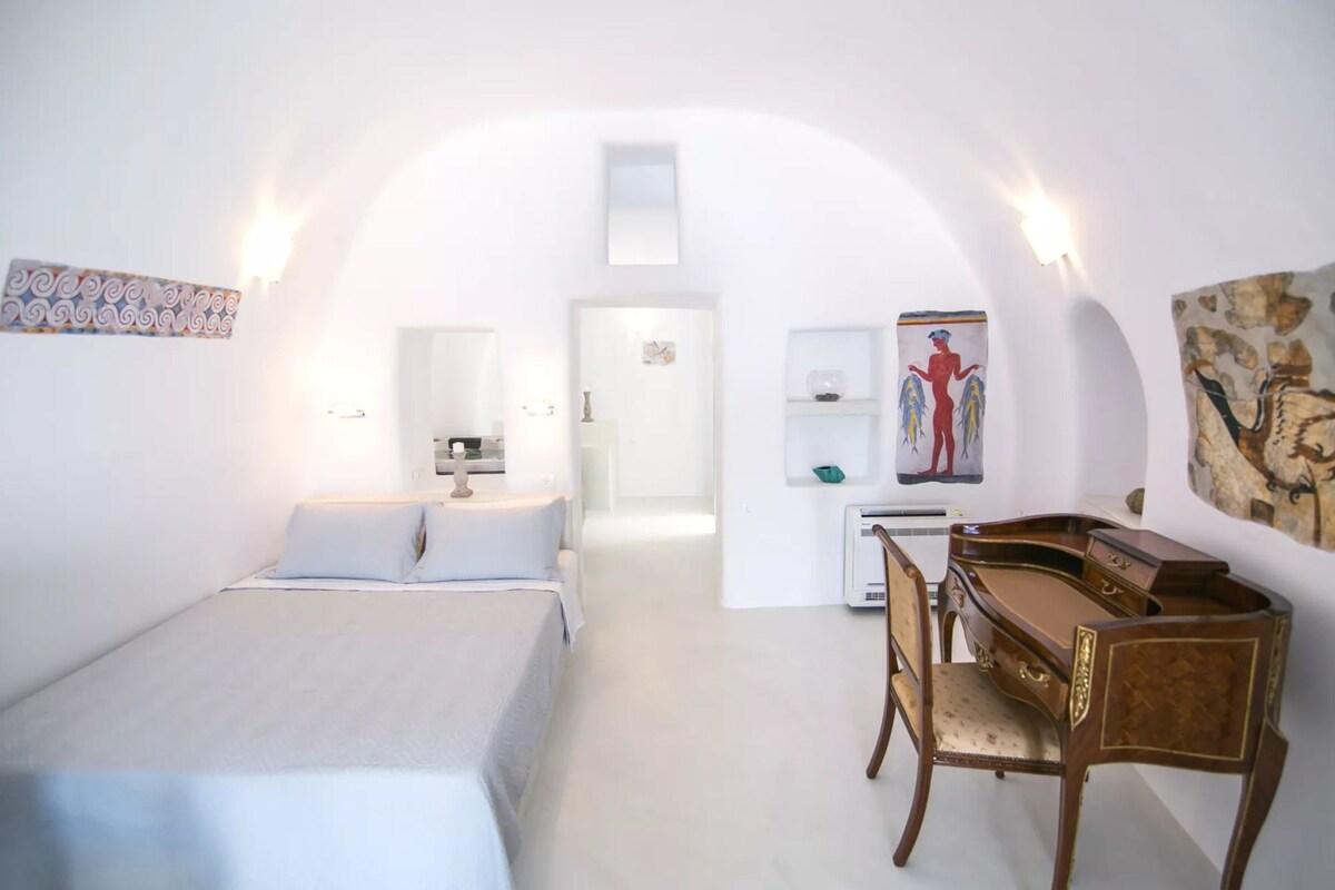 A room with a bed, a desk, and a piano. There is a mirror and a painting on the wall.