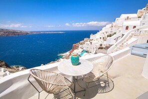 A terrace with a table and chairs overlooking a coastal village with white buildings and the sea. - Kastro Oia Houses  (Santorini)