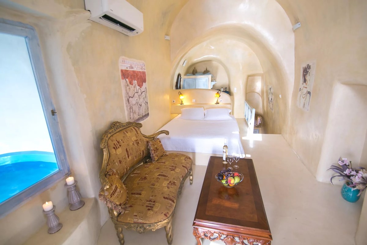 A room with a bed, a sofa, a table with fruit, and a window.