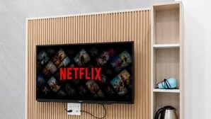 Un salon moderne avec un téléviseur fixé au mur affichant le logo de Netflix, une étagère intégrée avec une bouilloire et un climatiseur blanc.