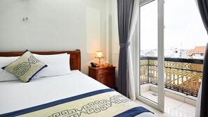Une chambre d’hôtel avec un lit, une table de chevet avec une lampe, une fenêtre avec des rideaux et une vue sur les bâtiments à l’extérieur.