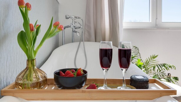 Una bandeja con un florero de tulipanes, un bol de fresas y dos copas de vino tinto sobre una cama.