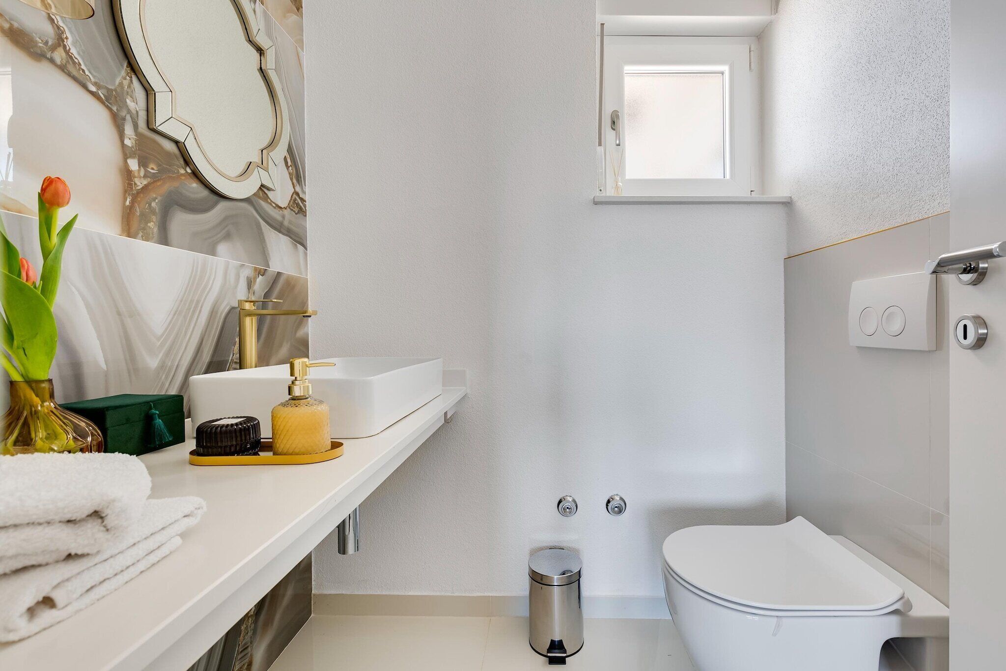 Ein modernes Badezimmer mit einem Marmor-Waschtisch, einer Toilette und einem kleinen Fenster.