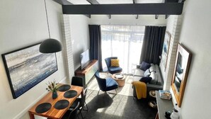 A modern living room with a dining area, a sofa set, a TV, and a large window.