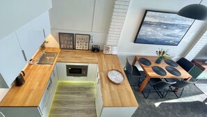 A modern kitchen with a microwave, kettle, and toaster. There is a dining area with a table and chairs, and a large window with a view of the city.
