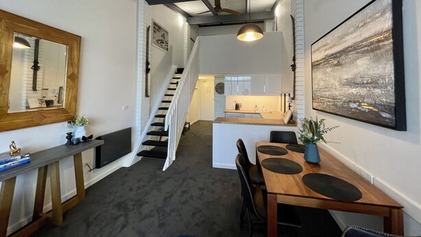 A modern kitchen with white cabinets, a wooden countertop, and a dining area with a wooden table and chairs.