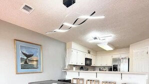 A modern kitchen with white cabinets, a dining area with a glass-top table and wicker chairs, and a ceiling with recessed lighting. - 2BDR/2.5BTH, located less than 2 miles from Canyon Lake. Hot-tub, stunning views, nearby golf course (Canyon Lake)
