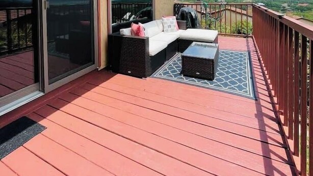 A covered outdoor deck with a red wooden floor, a black wicker sofa, and a small table. - 2BDR/2.5BTH, located less than 2 miles from Canyon Lake. Hot-tub, stunning views, nearby golf course (Canyon Lake)