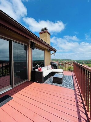A covered outdoor deck with a red wooden floor, a black wicker sofa, and a small table. - 2BDR/2.5BTH, located less than 2 miles from Canyon Lake. Hot-tub, stunning views, nearby golf course (Canyon Lake)