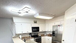 A modern kitchen with white cabinets, a stainless steel refrigerator, a microwave, and a stove. There is a long island with stools and a built-in sink. - 2BDR/2.5BTH, located less than 2 miles from Canyon Lake. Hot-tub, stunning views, nearby golf course (Canyon Lake)