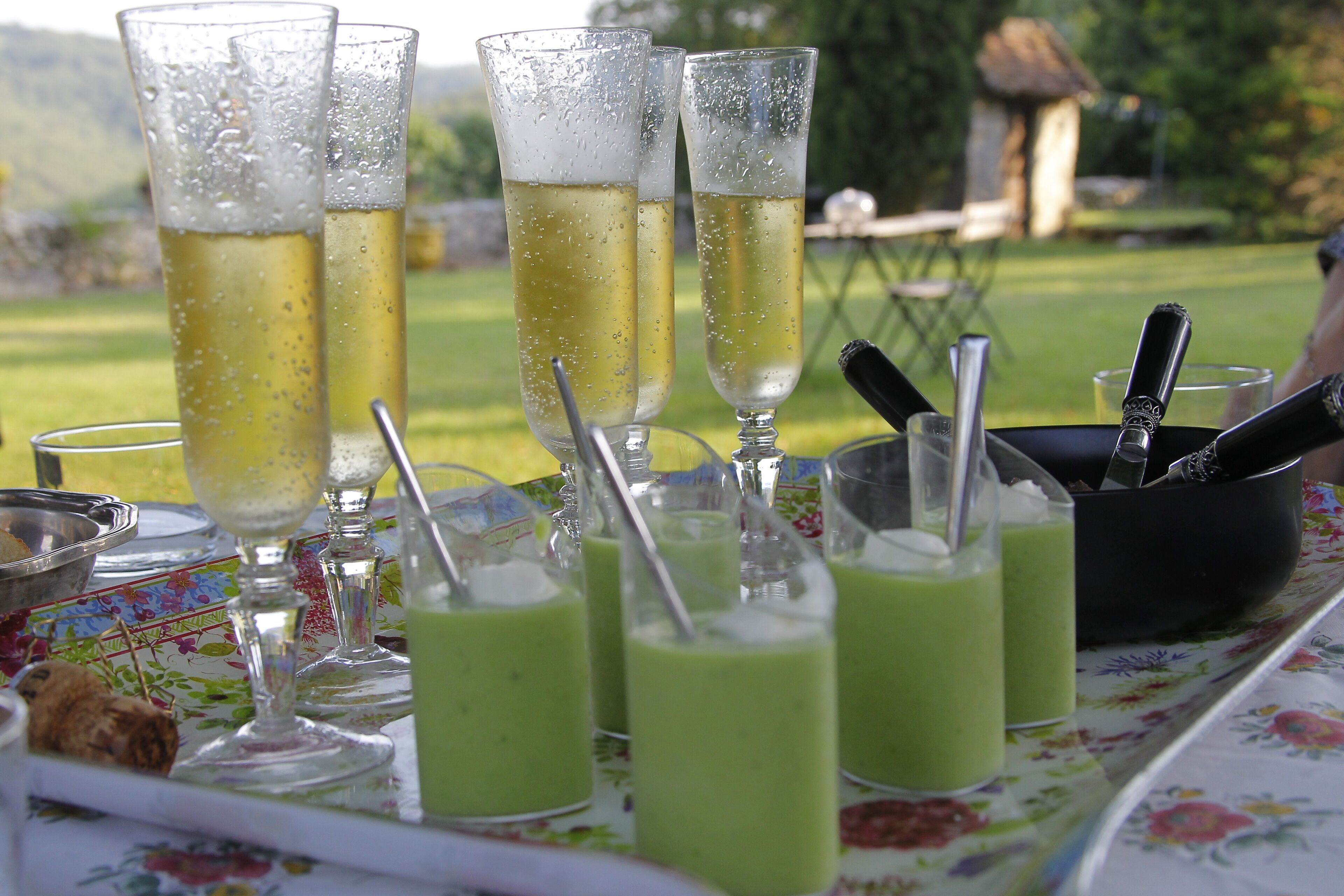 A table with champagne glasses and green drinks, a bottle of champagne, and a bowl of nuts.