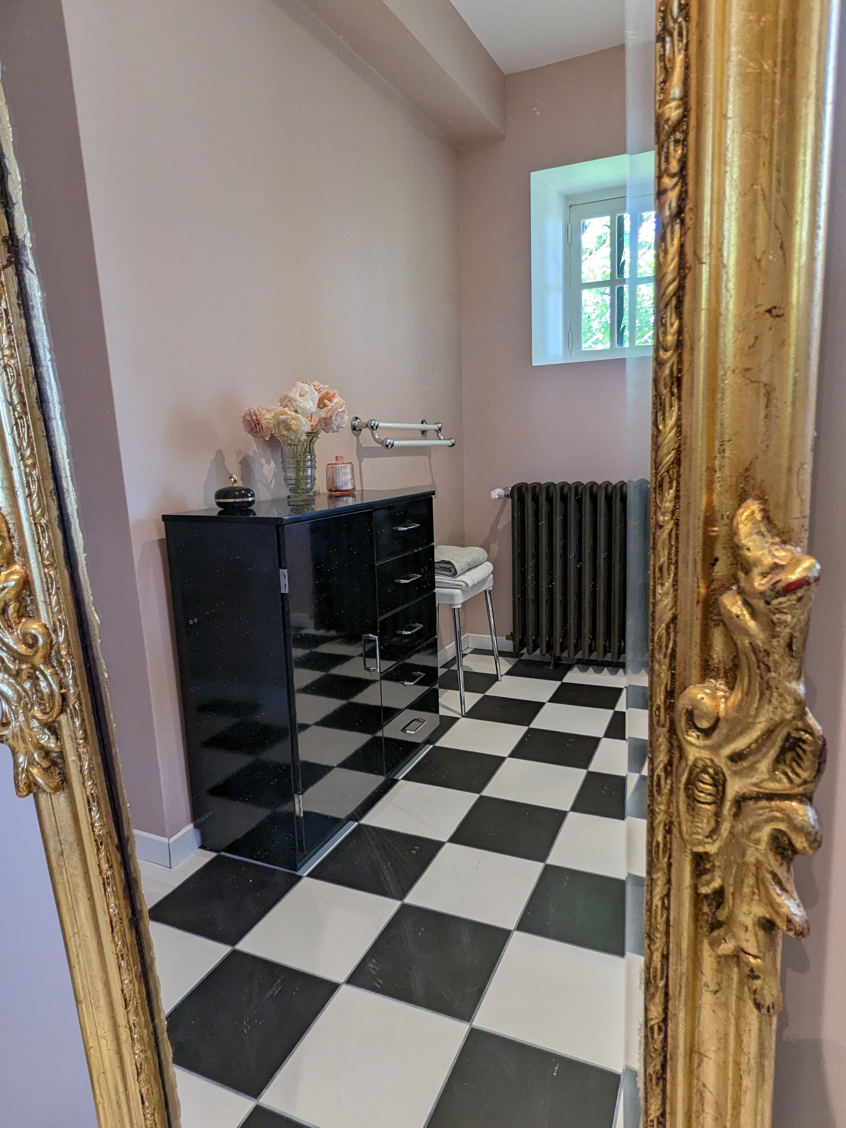 Une salle de bain avec un sol à carreaux noirs et blancs, un meuble-lavabo noir avec un plateau en verre, un porte-serviettes blanc et un radiateur.
