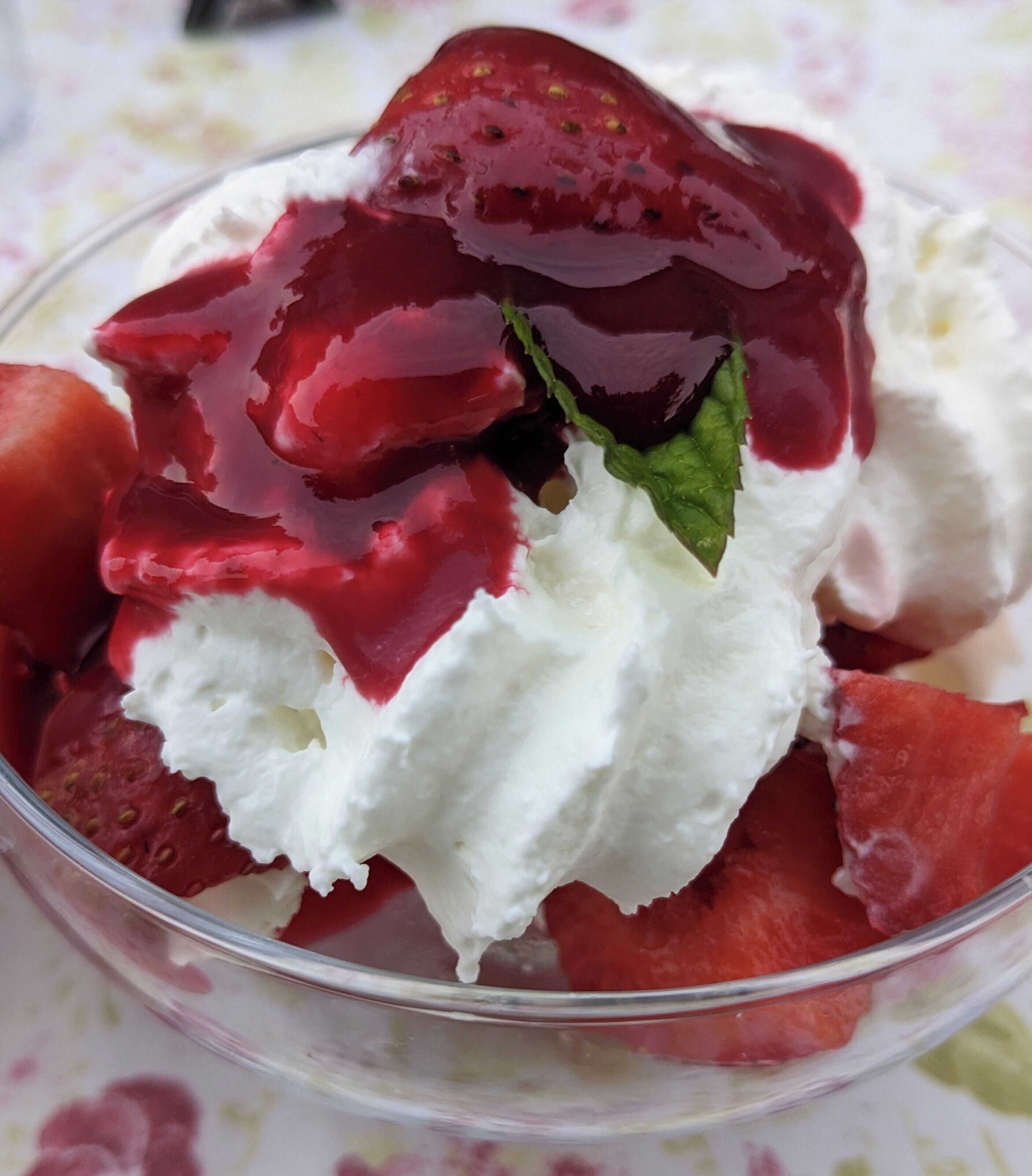 Un bol de dessert garni de crème fouettée, de fraises et d’une sauce rouge.