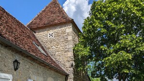 A stone building with a tiled roof, a dining table set outdoors with chairs, and a grassy area with trees. - Romantic french cottage 6 persons with pool, 15 min from Rocamadour/Dordogne (Reilhaguet)