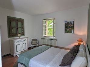 A bedroom with a bed, a chair, a dresser, a window, and a radiator.